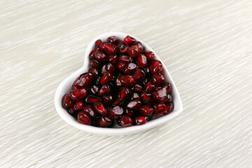 White plate in the shape of a heart with pomegranate fruits on a light wooden background