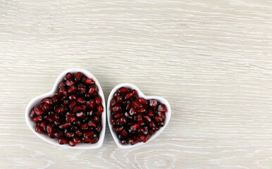 Two heart-shaped plates with pomegranate fruits on a light wooden background