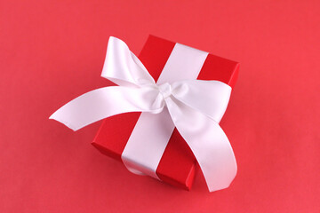 Red gift box with white ribbon on red background