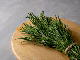 A bouquet of green rosemary tied with a whip on a wooden board. Grey background.