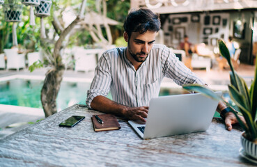Focused ethnic man working on project and browsing laptop