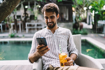 Happy man with bright drink using social media on smartphone