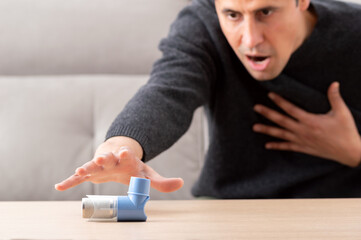 Man suffering asthma attack reaching inhaler sitting on a couch in the living room at home
