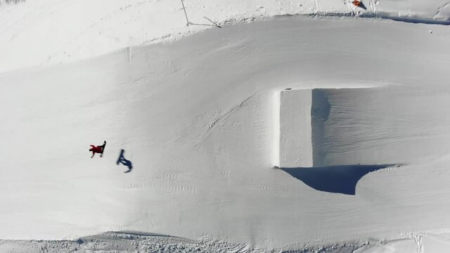 Snowboarder spinning off a jump in the snowpark with an aerial view
