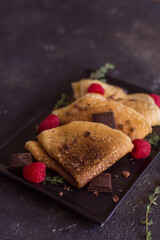 thin homemade pancakes with berries and chocolate on a dark background, close-up, vertical arrangement