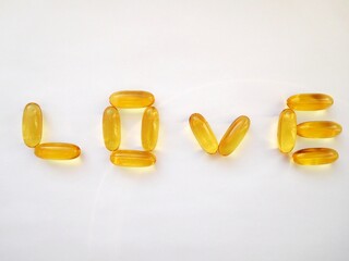 letters of the word love, lined with yellow capsules with vitamins A, E, D, omega 3 oil on a white...