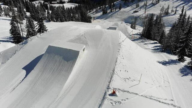 ski resort in the mountains with snowboarder spinning off a jump in the snowpark