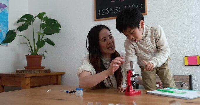 Happy asian mother and little son using microscope at home - School education, family and science concept