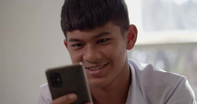 An Asian male high school student in a white school uniform is enjoying a happy smile on his smartphone on the Internet and social media.