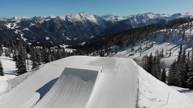 ski resort in the mountains with a snowpark, skier jumping inverted off a jump