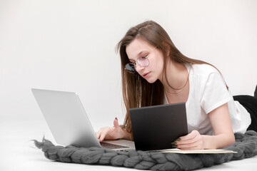 Naklejka premium A seriously young girl in glasses sits with a laptop. Education, remote work and blogging. Isolated on a white background.