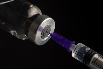 Close-up of filling a syringe with vaccine on a black background. A syringe with a needle draws the medicine.