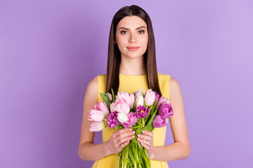 Portrait of attractive long-haired girl holding in hands tulips greetings isolated over violet purple pastel color background