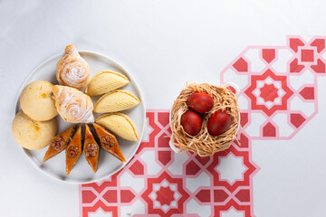 Beautiful Novruz table set up with national pastry in white plate with dyed red eggs and flowers in red and white colors. Celebration of spring equinox in Azerbaijan in March. Flat lay  copy space