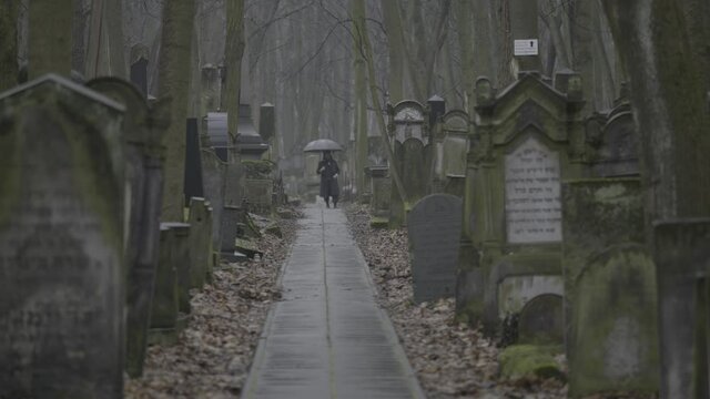 A telephoto of a huge Jewish cemetery, where an Orthodox Jew is standing, holding an umbrella and waiting for someone, the focus changes from the graves back to him. a 4K (S-Log) clip, Warsaw, Poland.