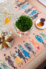Obraz na płótnie Canvas Beautiful Novruz table set up in pastel colors with wheat grass - semeni, satin ribbon, traditional pastry. National holiday, celebration of spring equinox