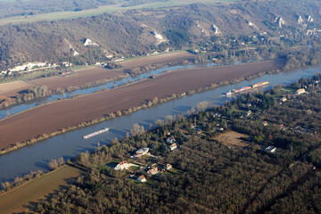 Barges and transport boats on the Seine river seen from the sky at Haute-Isle en Vexin