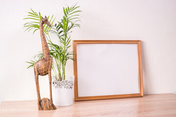 Portrait broun picture frame mockup on wooden table. Wooden decor giraffe figure and palm. White wall background. Scandinavian interior. 