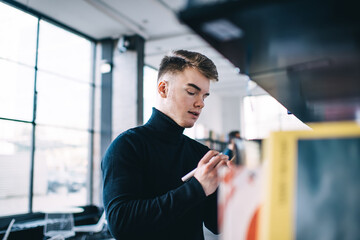 Stylish man taking note with pencil standing near bookcase