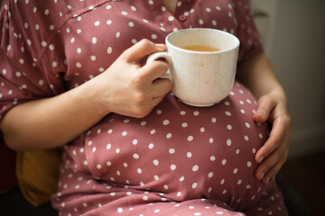 Pregnant woman holding cup of tea at home.