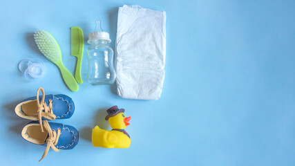 Baby care accessories, newborn baby diaper, pacifier, comb and hair brush, bottle, little boy shoes and toy on a blue background. Wish list or shopping overview for pregnancy, baby shower concept.