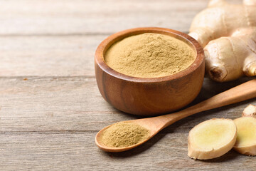 Ginger finely ground powder with rhizone and slices on wooden table.