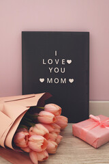 Beautiful tulips with the letter I LOVE MOM on letterboard sign. Pink background, frame, border. Lovely greeting card with tulips for Mothers day, wedding or happy event concepts