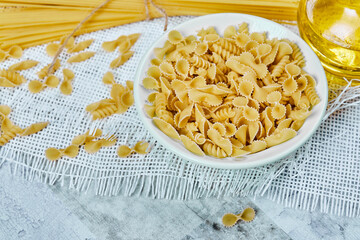 A bowl of uncooked pasta and spaghetti on a marble background