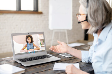A schoolgirl on a laptop screen is listening attentively to the teacher, learning online on the...