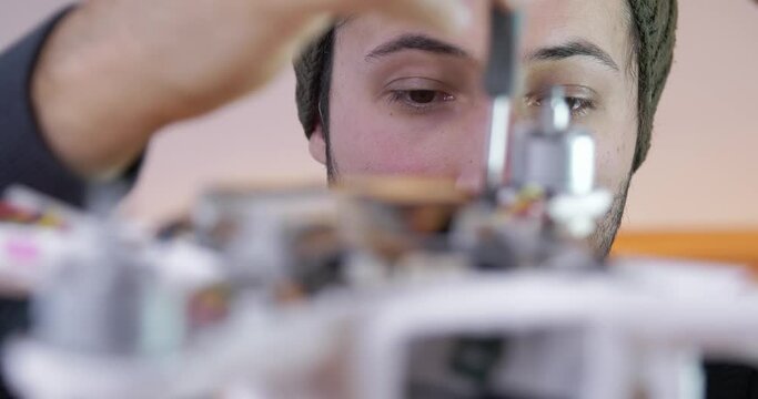 Focus on the eyes of a man who is assembled with a screwdriver drone. Radial camera movement.