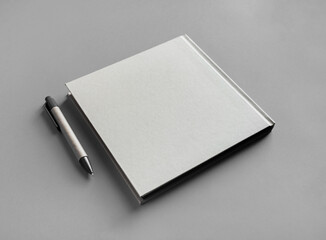 Closed blank square brochure and pen on gray paper background.