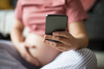Pregnant woman sitting on floor at home and using mobile phone