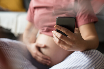 Pregnant woman sitting on floor at home and using mobile phone