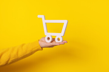 shopping cart on hand over yellow background