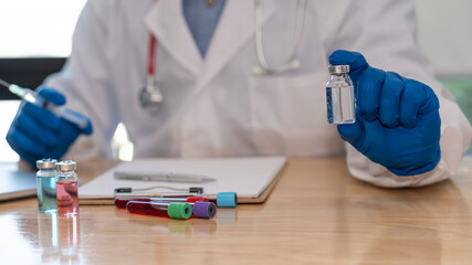 Doctors hold a vial of COVID-19 vaccine in a blue rubber glove in a close-up laboratory. Study the concept of coronavirus vaccination. On the table there was a bottle of experimental medicine and a no