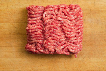 A briquette of raw minced beef on a battered cutting board