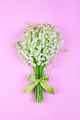 bouquet of lily of the valley flowers with a green bow on a pink background close-up