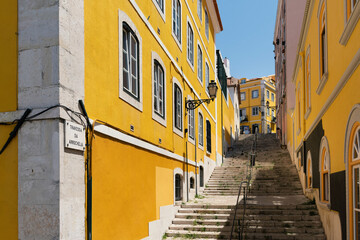 Fototapeta na wymiar Staircase alley in the old town of Lisbon with yellow picturesque house facades.