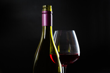 Wine bottle and glass with red wine on dark glossy background.