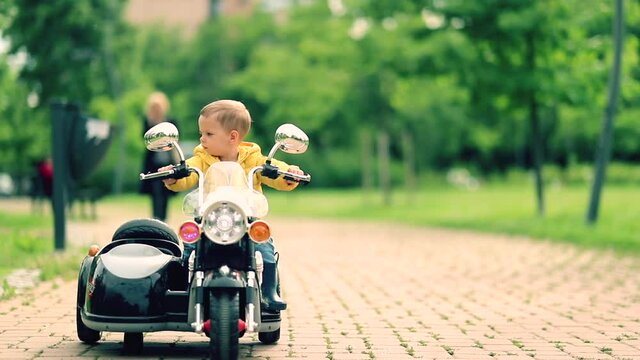 Happy little boy driving a toy motorcycle in a park