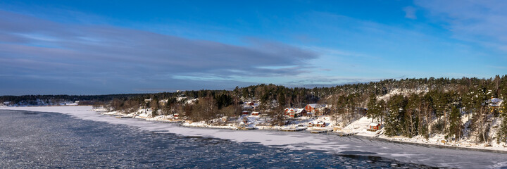 Beautiful view of the northern snow ice covered coast of the Baltic sea in winter day. Panorama of the shores of Scandinavia Sweden or Finland from cruise ship. Forestry islands on the horizon.