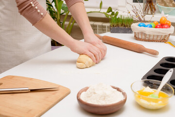 Obraz na płótnie Canvas the process of rolling out the dough at home on the table is the hands of a woman for making cruffins festive pastries for Easter . side view of a bright kitchen , with painted eggs