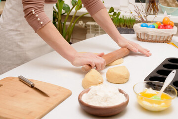 Obraz na płótnie Canvas the process of rolling out the dough at home on the table is the hands of a woman for making cruffins festive pastries for Easter . side view of a bright kitchen , with painted eggs