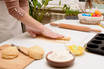 the process of rolling out the dough at home on the table is the hands of a woman for making cruffins festive pastries for Easter . side view of a bright kitchen , with painted eggs