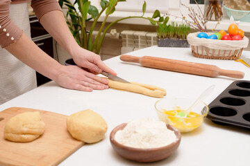 the process of rolling out the dough at home on the table is the hands of a woman for making cruffins festive pastries for Easter . side view of a bright kitchen , with painted eggs