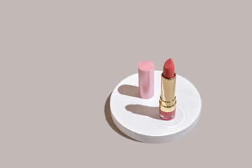 Pink lipstick on a white round podium with shadows on a beige natural background. Wabisabi style, earth tone. Mockup for the presentation of cosmetics.