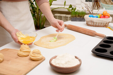 the process of rolling out the dough at home on the table is the hands of a woman for making cruffins festive pastries for Easter . side view of a bright kitchen , with painted eggs