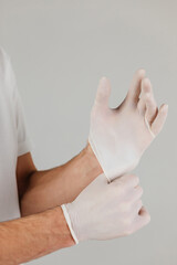 Fototapeta premium Man in white clothes and protective respirator wears white medical gloves on his hands. Studio photo on grey background.