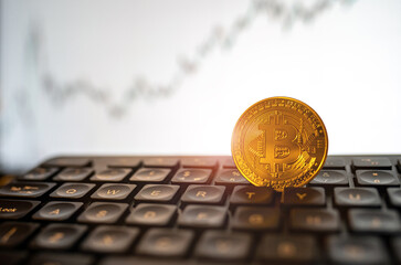 Gold shining Bitcoin coin on keyboard with raising graph. Cryptocurrency, mining, stock concept