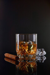 Whiskey with ice or brandy in glass with cigar on black background. Whisky with ice in glass. Whiskey or brandy. Selective focus.